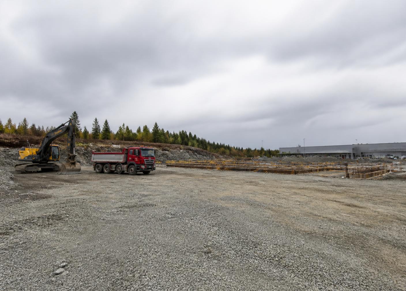 Illustrasjonsbilde: planert grunn med gravemaskin og lastebil foran et næringsbygg under oppføring.